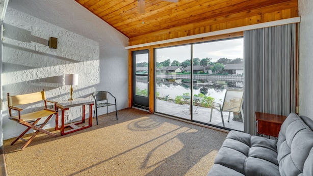 A room with a wooden ceiling, a large sliding glass door to a courtyard, a grey sofa, and a wooden chair. - Waterfront Haines City Vacation Rental w/ Pool! (Haines City)