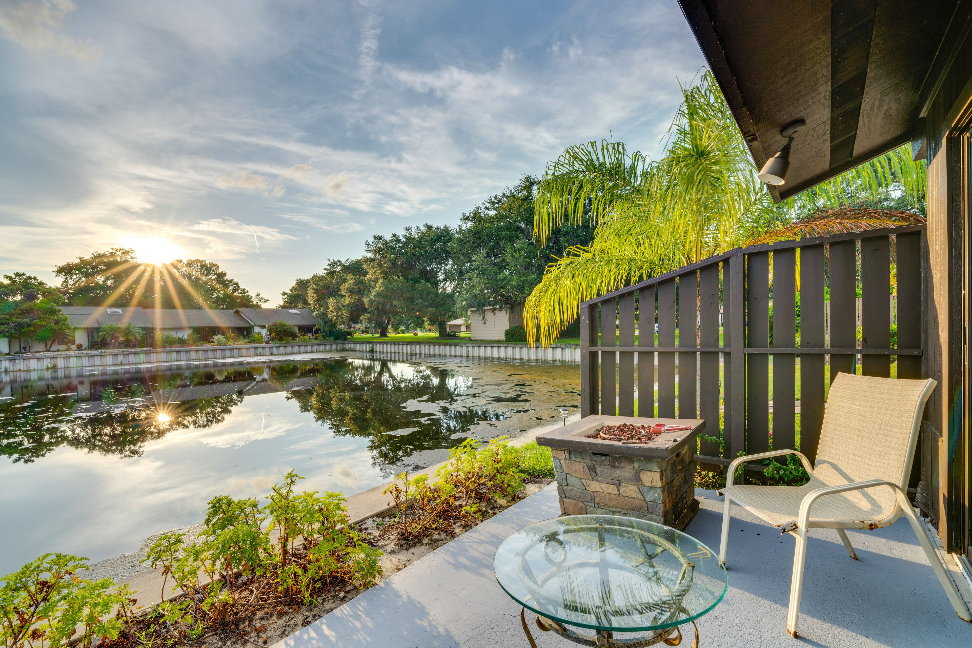 Une terrasse extérieure paisible, avec une table en verre, un fauteuil en osier et un petit foyer.