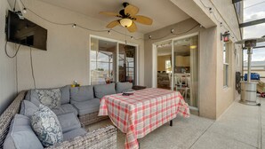 A covered outdoor seating area with a sofa, a table with a checkered tablecloth, a ceiling fan, and a TV mounted on the wall. - Lanai w/ Private Pool! Golf Getaway in Haines City (Haines City)