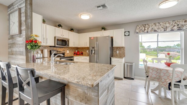 A kitchen with granite countertops, white cabinets, a stainless steel refrigerator, and a dining area with a table and chairs. - Lanai w/ Private Pool! Golf Getaway in Haines City (Haines City)
