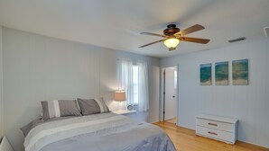 A bedroom with a bed, a nightstand, a dresser, a ceiling fan, and three wall-mounted paintings.