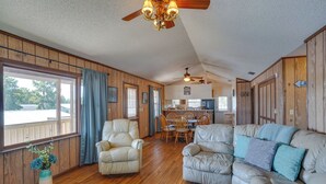 A spacious living room with a wooden floor, a large sofa, a dining table with chairs, and a ceiling fan.