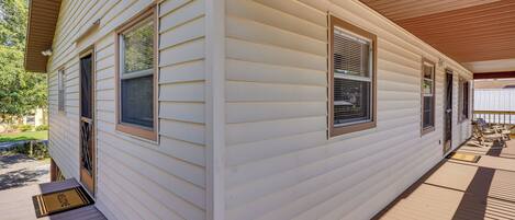 A single-story house with a covered porch, a front door, and two windows with shutters.