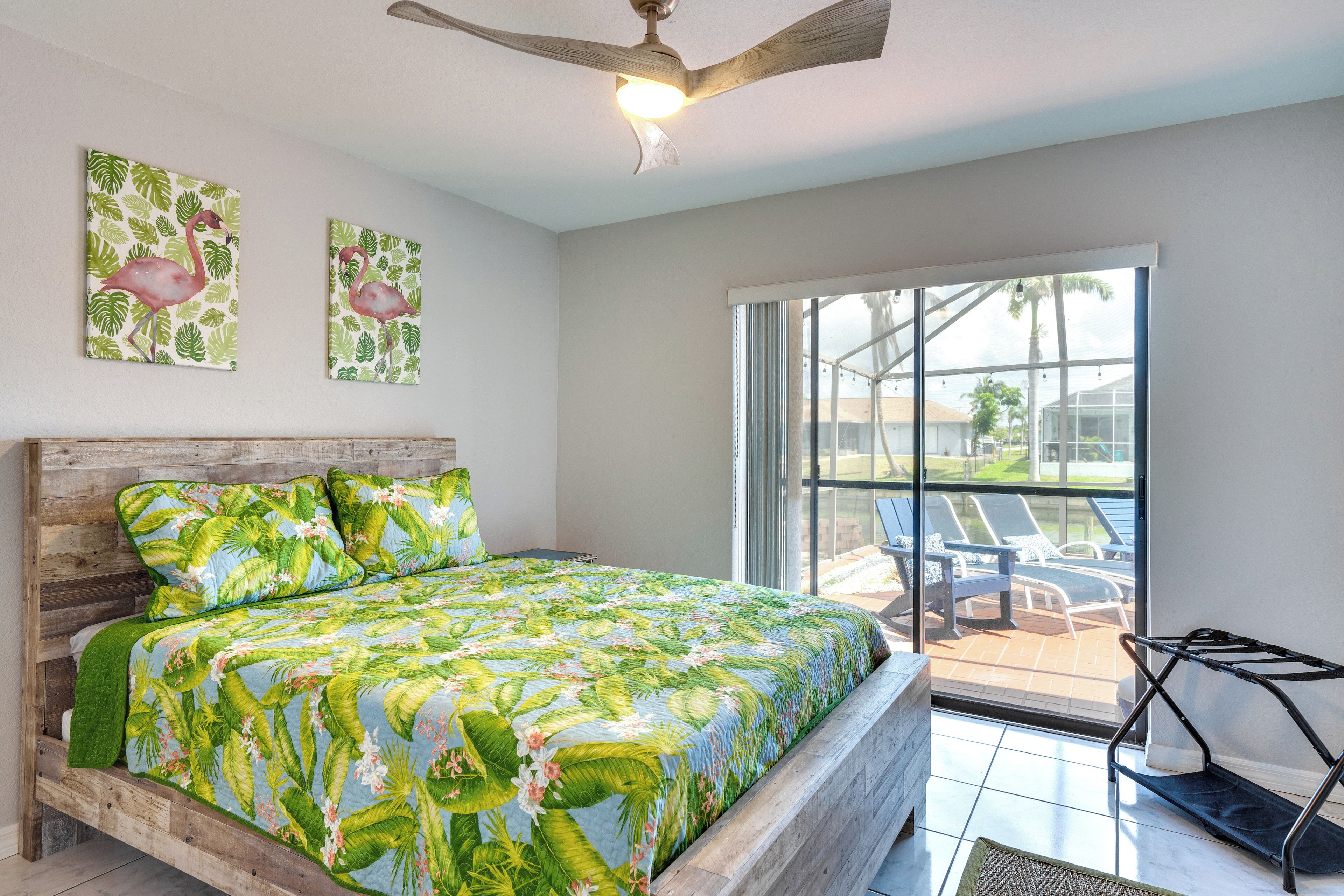 A bedroom with a wooden bed, a ceiling fan, and a large window with a view of outdoor chairs.