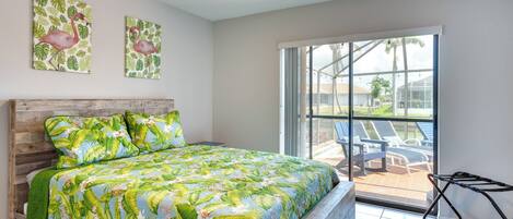 A bedroom with a wooden bed, a ceiling fan, and a large window with a view of outdoor chairs.