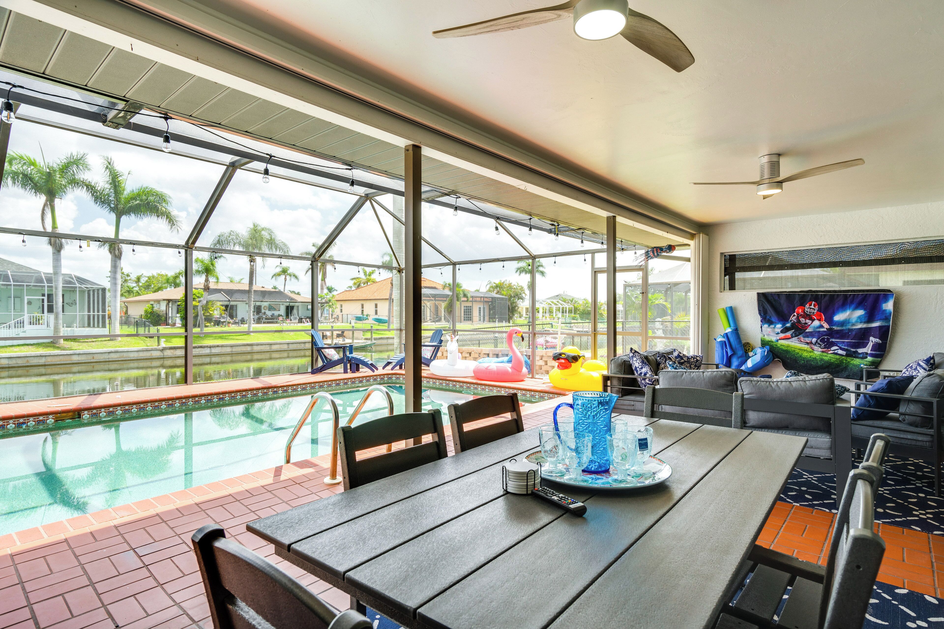 Un espace repas aménagé au bord de la piscine, avec une table, des chaises et un écran de télévision.
