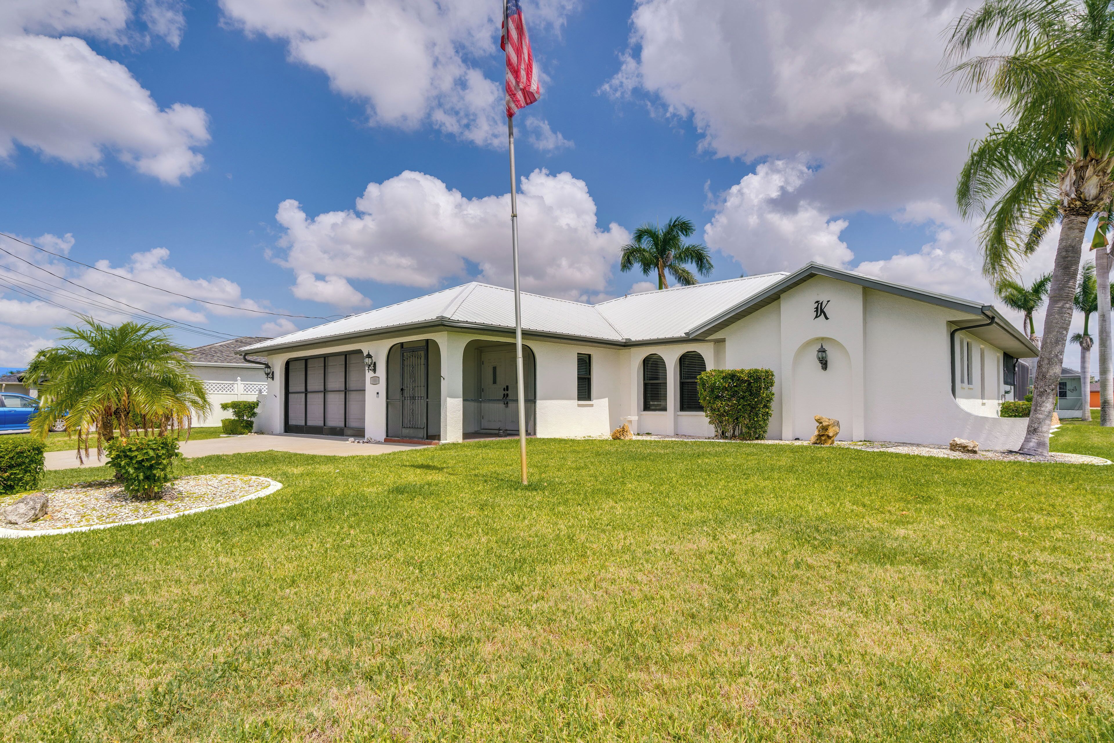 A white building with a flagpole, palm trees, and a well-maintained lawn.
