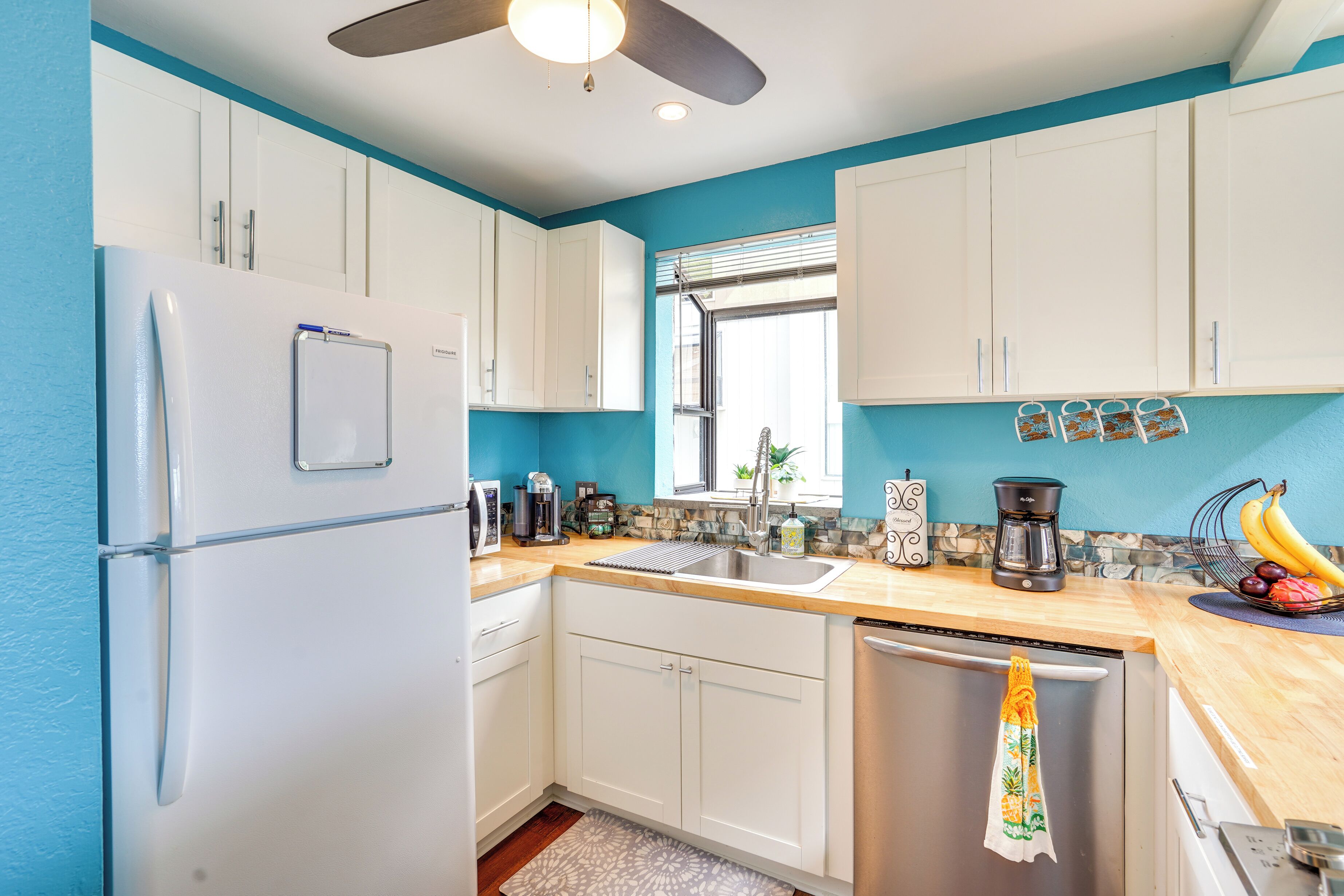 Cozinha com armários brancos, geladeira de aço inoxidável, cafeteira e escorredor de louça.