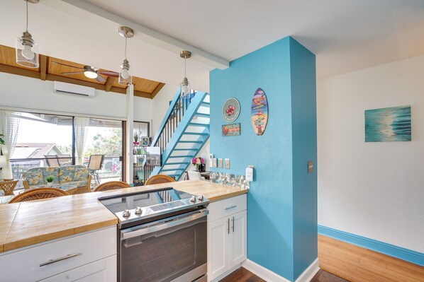 A kitchen with a wooden countertop, stainless steel appliances, a blue accent wall, and a staircase with a blue railing.