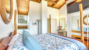 Ein Schlafzimmer mit Holzboden, einem großen Bett mit floralem Bettzeug, einem Spiegel und einem Fernseher.