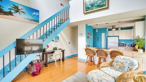Eine moderne Wohnung mit einer Holztreppe, einer Küche mit weißen Schränken, einem Essbereich mit Korbmöbeln und einem Wohnzimmer mit Flachbildfernseher.