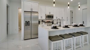 A modern kitchen with white cabinetry, stainless steel appliances, and bar stools. - Furnished Lanai & Private Pool: Cape Coral Home (Cape Coral)