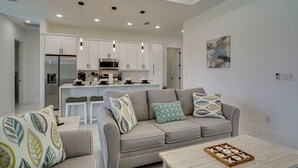 A modern living room with a grey sofa, patterned cushions, a wooden coffee table, and a kitchen in the background. - Furnished Lanai & Private Pool: Cape Coral Home (Cape Coral)