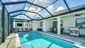 A swimming pool with a glass ceiling, lounge chairs, a grill, and a ceiling fan. - Furnished Lanai & Private Pool: Cape Coral Home (Cape Coral)