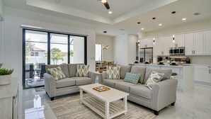 A modern living room with a sofa set, a coffee table, and a kitchen area with white cabinets and appliances. - Furnished Lanai & Private Pool: Cape Coral Home (Cape Coral)