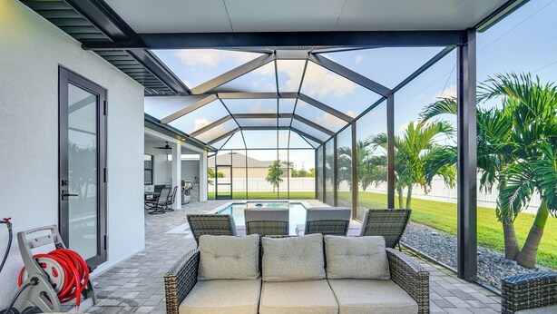 A covered outdoor seating area with a pool in the background. - Furnished Lanai & Private Pool: Cape Coral Home (Cape Coral)