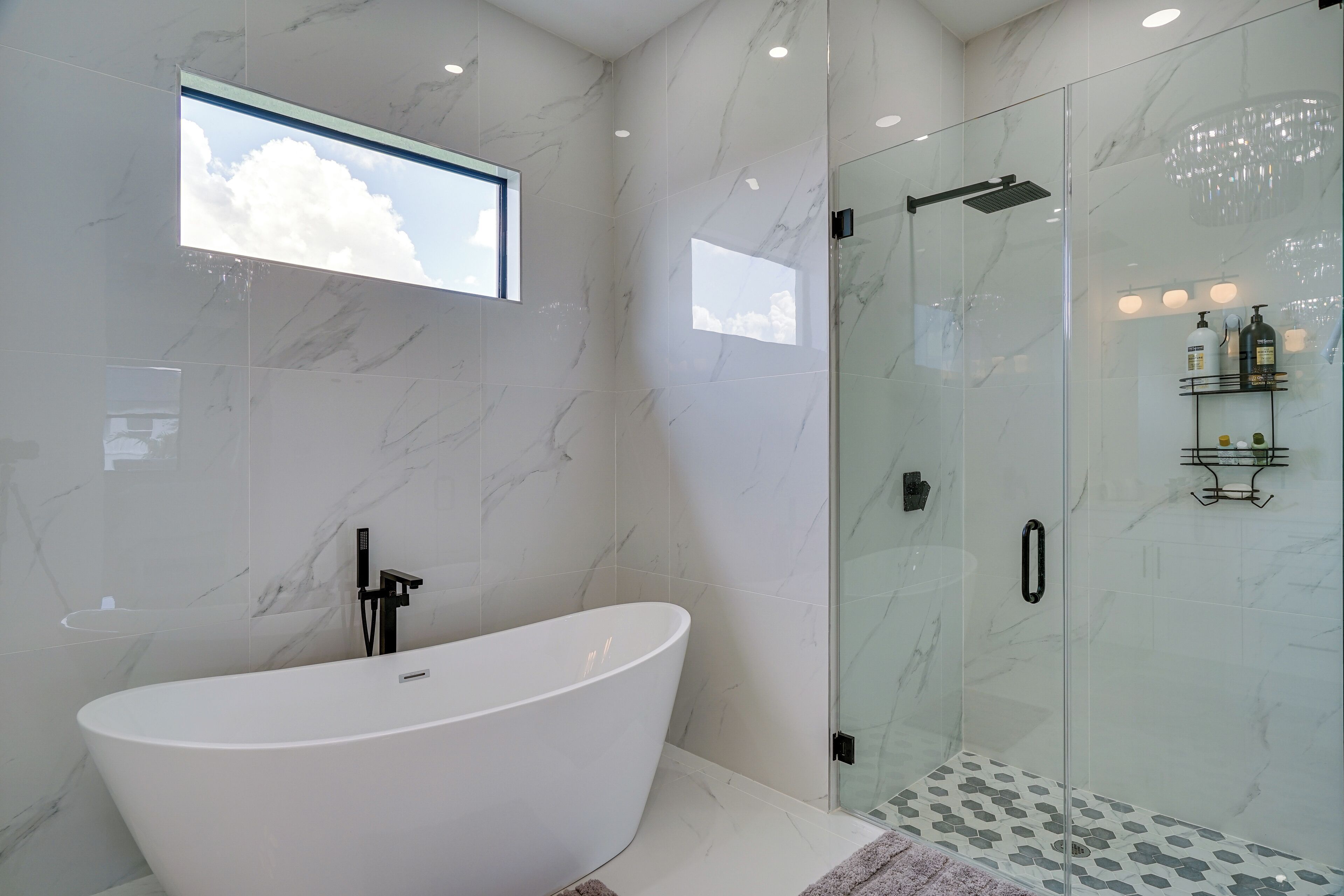 A modern bathroom with a freestanding bathtub, a glass-enclosed shower, and a small window.