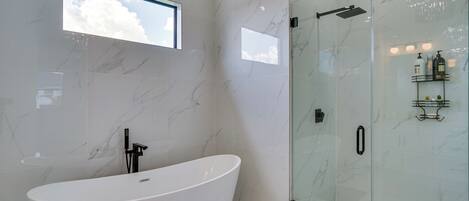 A modern bathroom with a freestanding bathtub, a glass-enclosed shower, and a small window.