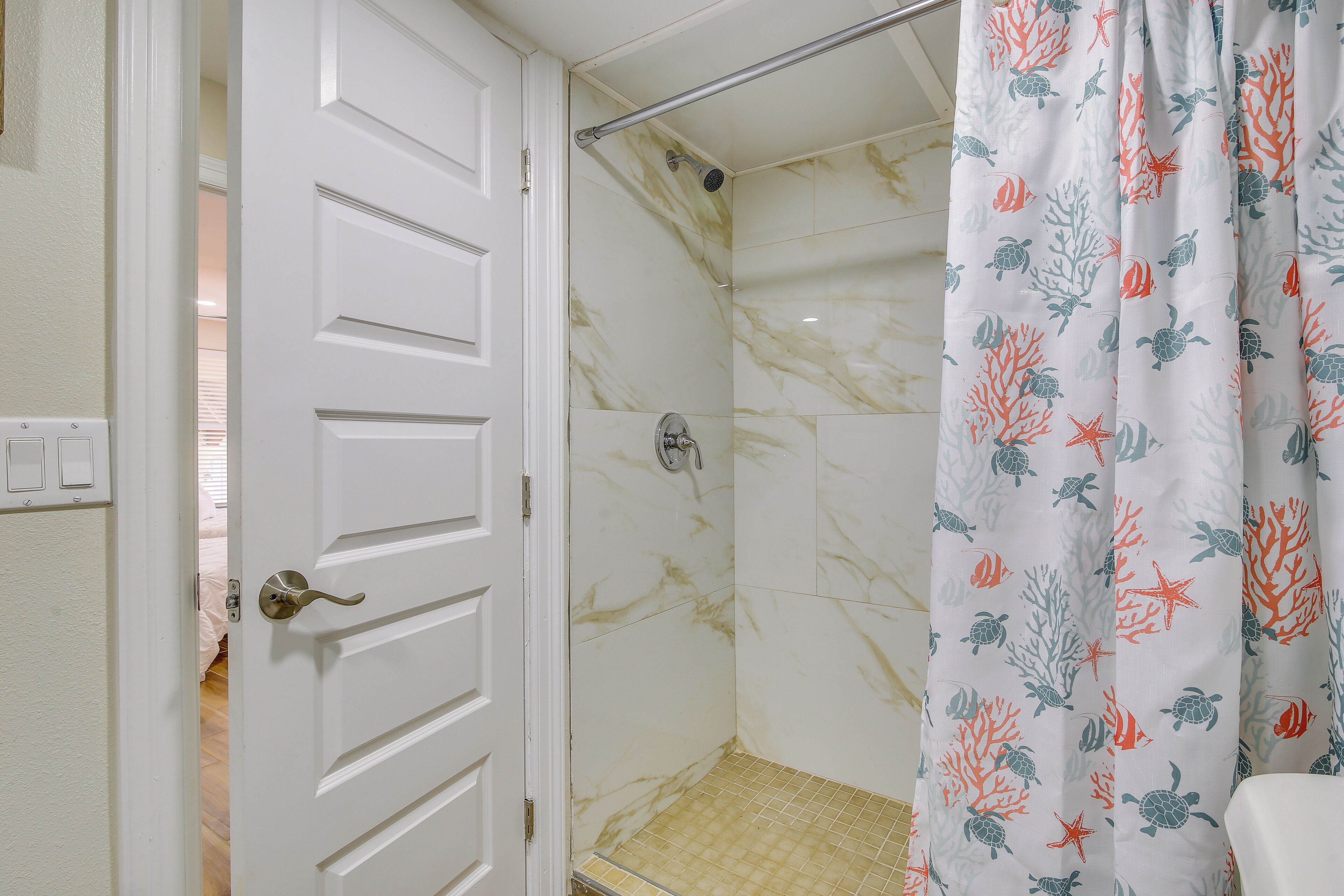 A bathroom with a shower, a door, and a curtain with a marine life pattern.