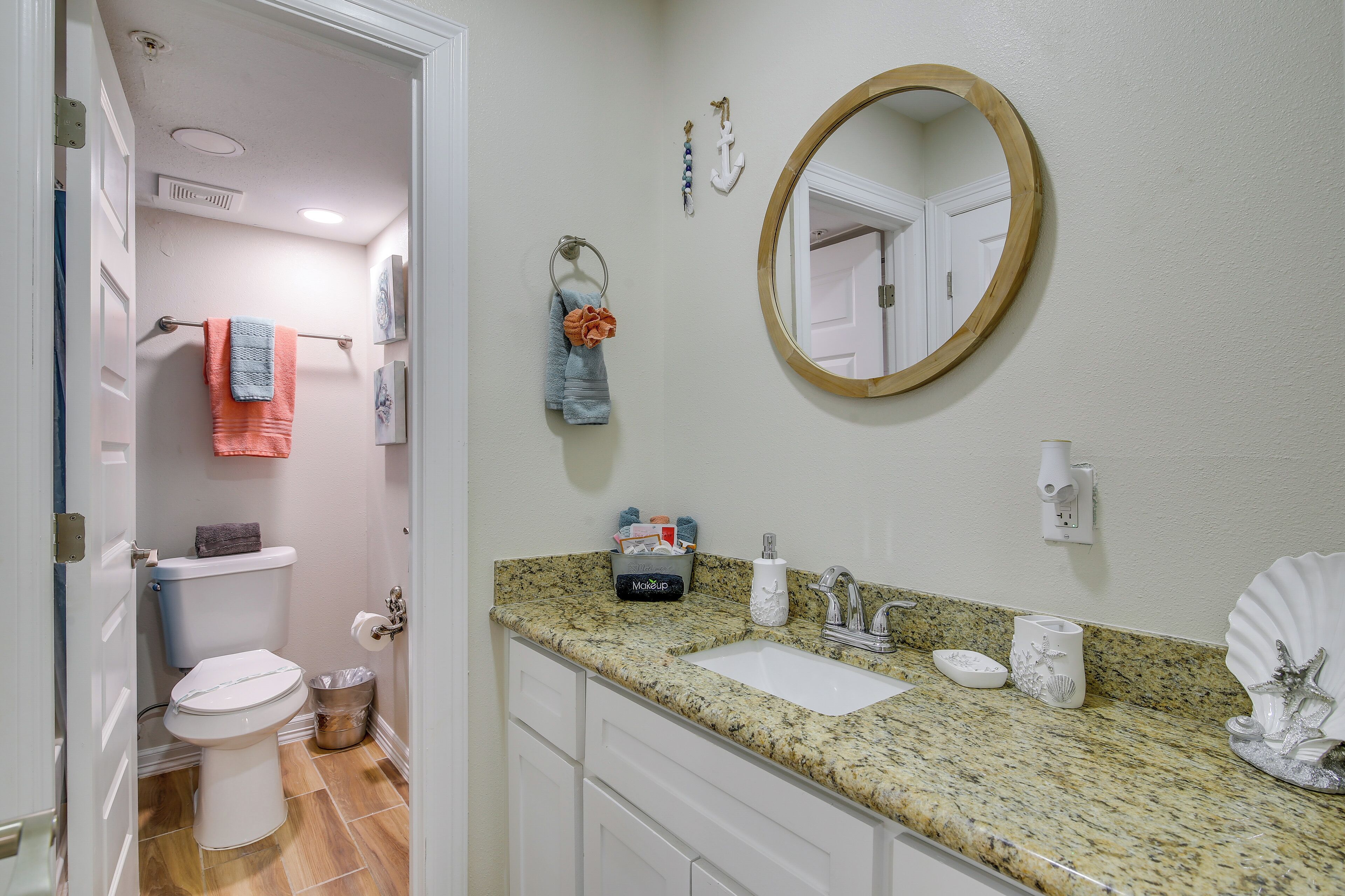 A bathroom with a toilet, sink, and mirror. There are towels hanging on a rack, and a trash can is visible.