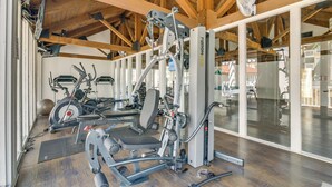 A gym with various exercise equipment, wooden beams on the ceiling, and large windows. - South Padre Island Condo: Walk to the Beach! (South Padre Island)