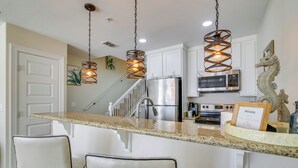 A kitchen with a granite countertop, white cabinets, stainless steel appliances, and a hanging light fixture. - South Padre Island Condo: Walk to the Beach! (South Padre Island)
