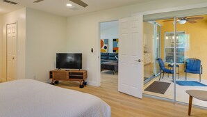 A bedroom with a bed, a TV on a wooden stand, and a door leading to a balcony with chairs and a table. - Heated Pool: Pet-friendly Home in Cape Coral (Cape Coral)