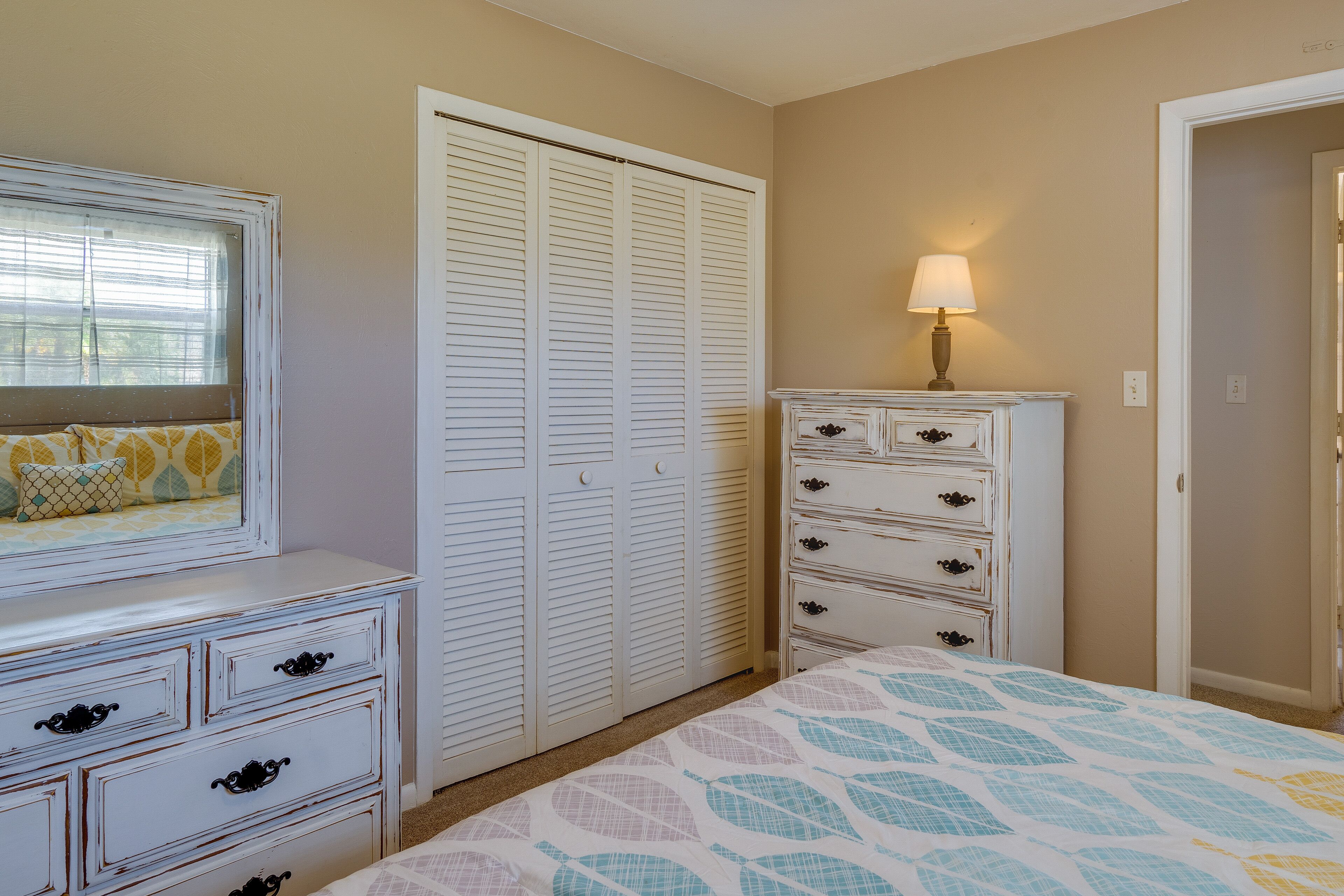 Un dormitorio con cama, cómoda, armario y mesita de noche con lámpara.