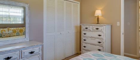 Un dormitorio con cama, cómoda, armario y mesita de noche con lámpara.