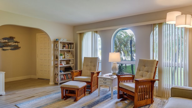 A spacious living room with wooden furniture, a bookshelf, and large windows with curtains. - Cape Coral Home w/ Private Heated Pool & Lanai! (Cape Coral)