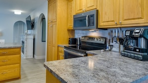 A kitchen with wooden cabinets, a stainless steel microwave, an oven, and a coffee maker. - Cape Coral Home w/ Private Heated Pool & Lanai! (Cape Coral)