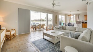 A spacious living area with a sofa, coffee table, and wicker chairs. There is a sliding glass door leading to a balcony with outdoor furniture. - Waterfront Retreat w/ Pool on Caloosahatchee River (Cape Coral)