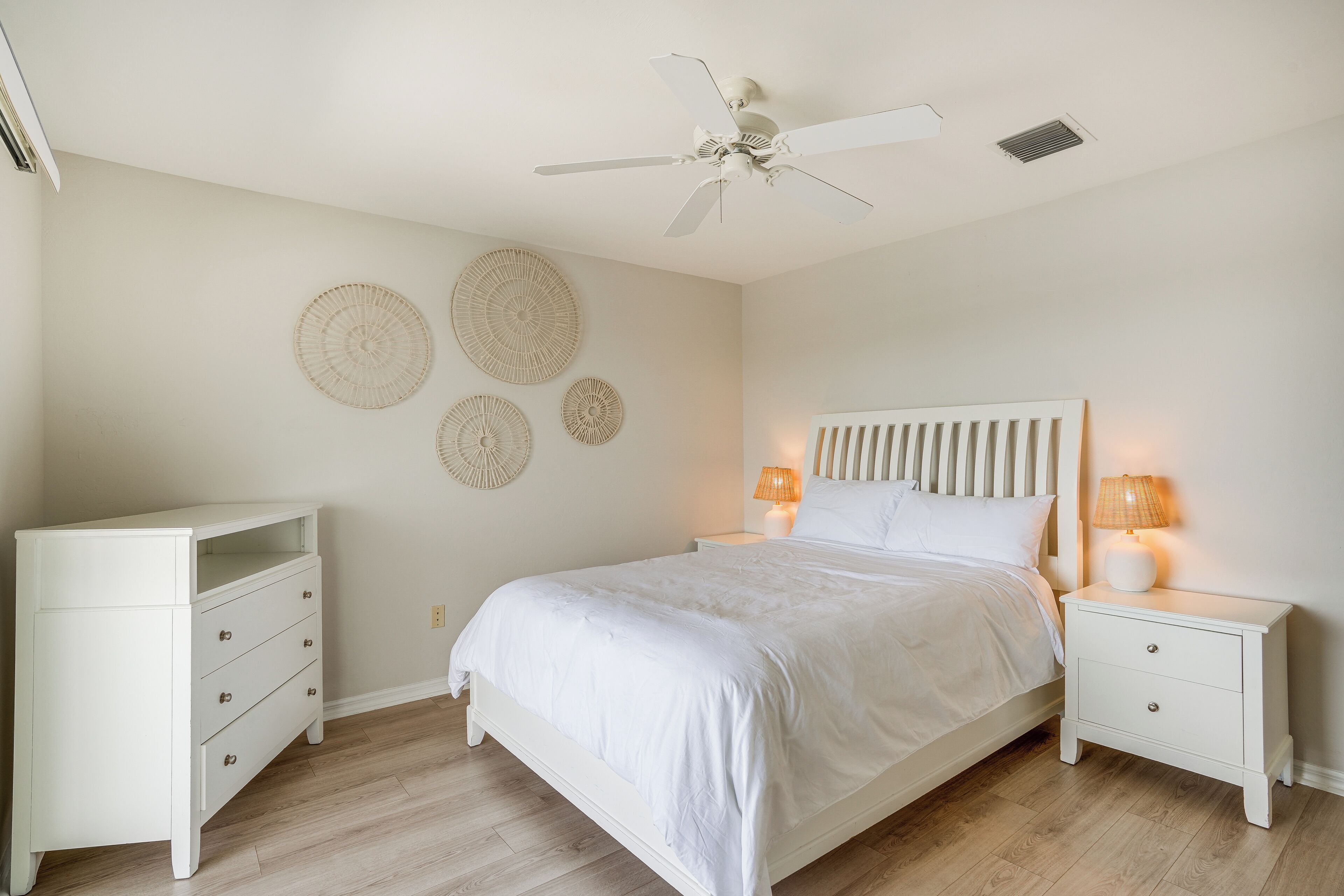 Une chambre à coucher comprenant un lit, des tables de chevet, un ventilateur de plafond et des éléments de décoration murale.