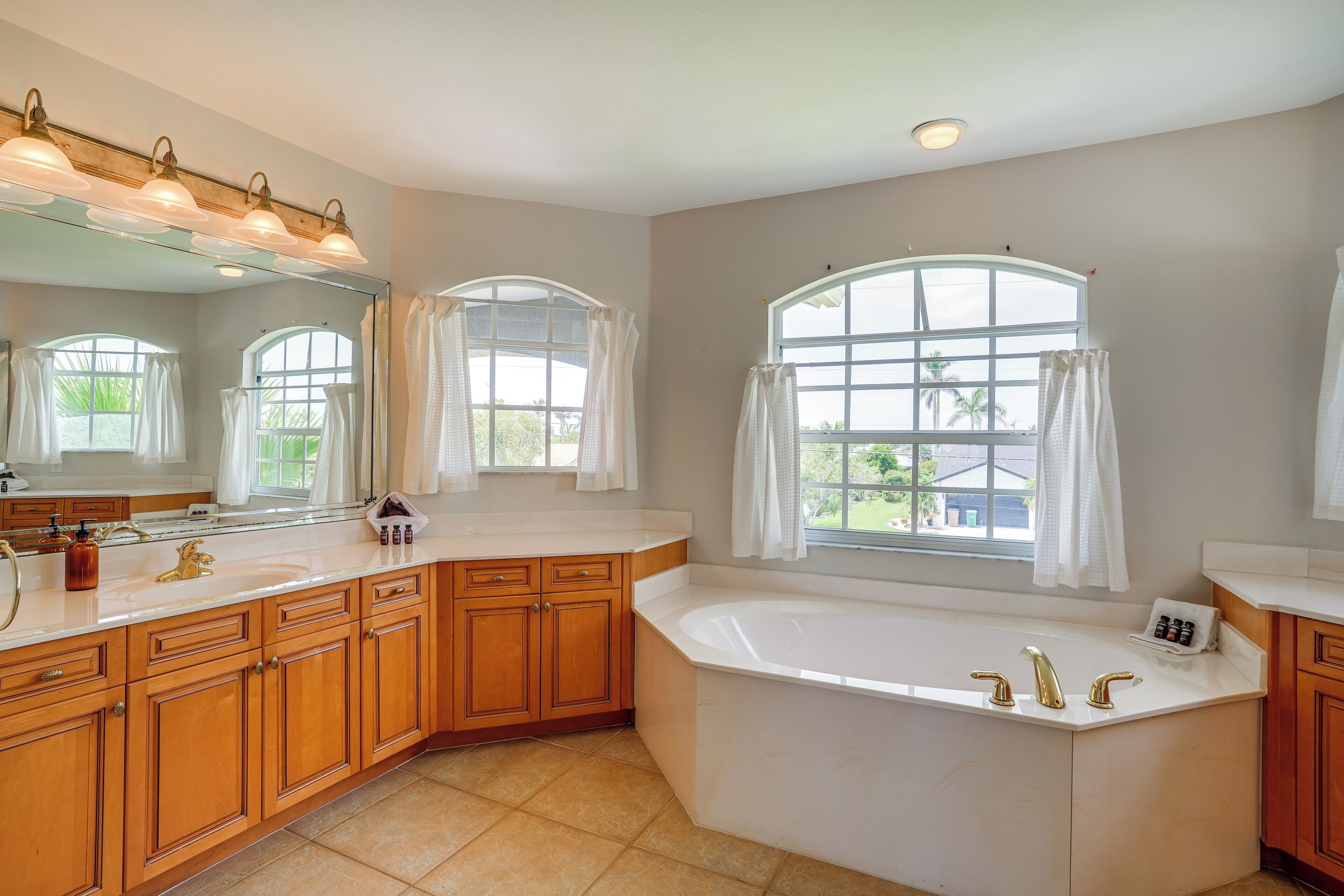 Un baño espacioso con una bañera grande, armarios de madera, tocador con lavabo y amplias ventanas que ofrecen luz natural.