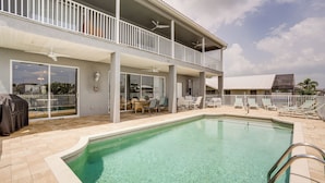 A swimming pool with a covered patio area, outdoor furniture, and a two-story building with balconies. - Waterfront Retreat w/ Pool on Caloosahatchee River (Cape Coral)