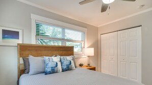 A bedroom with a large bed, a wooden headboard, a window with blinds, a nightstand with a lamp, and a closet with white doors. - Indian Rocks Beach Retreat: Walk to Beaches! (Indian Rocks Beach)
