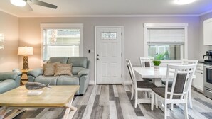 A modern living room with a grey sofa, a wooden coffee table, and a dining area with white chairs and a table. - Indian Rocks Beach Retreat: Walk to Beaches! (Indian Rocks Beach)