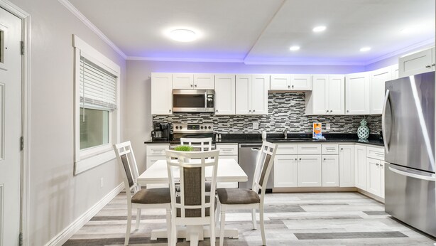 A modern kitchen with white cabinets, a stainless steel refrigerator, a microwave, and a tiled backsplash. - Indian Rocks Beach Retreat: Walk to Beaches! (Indian Rocks Beach)