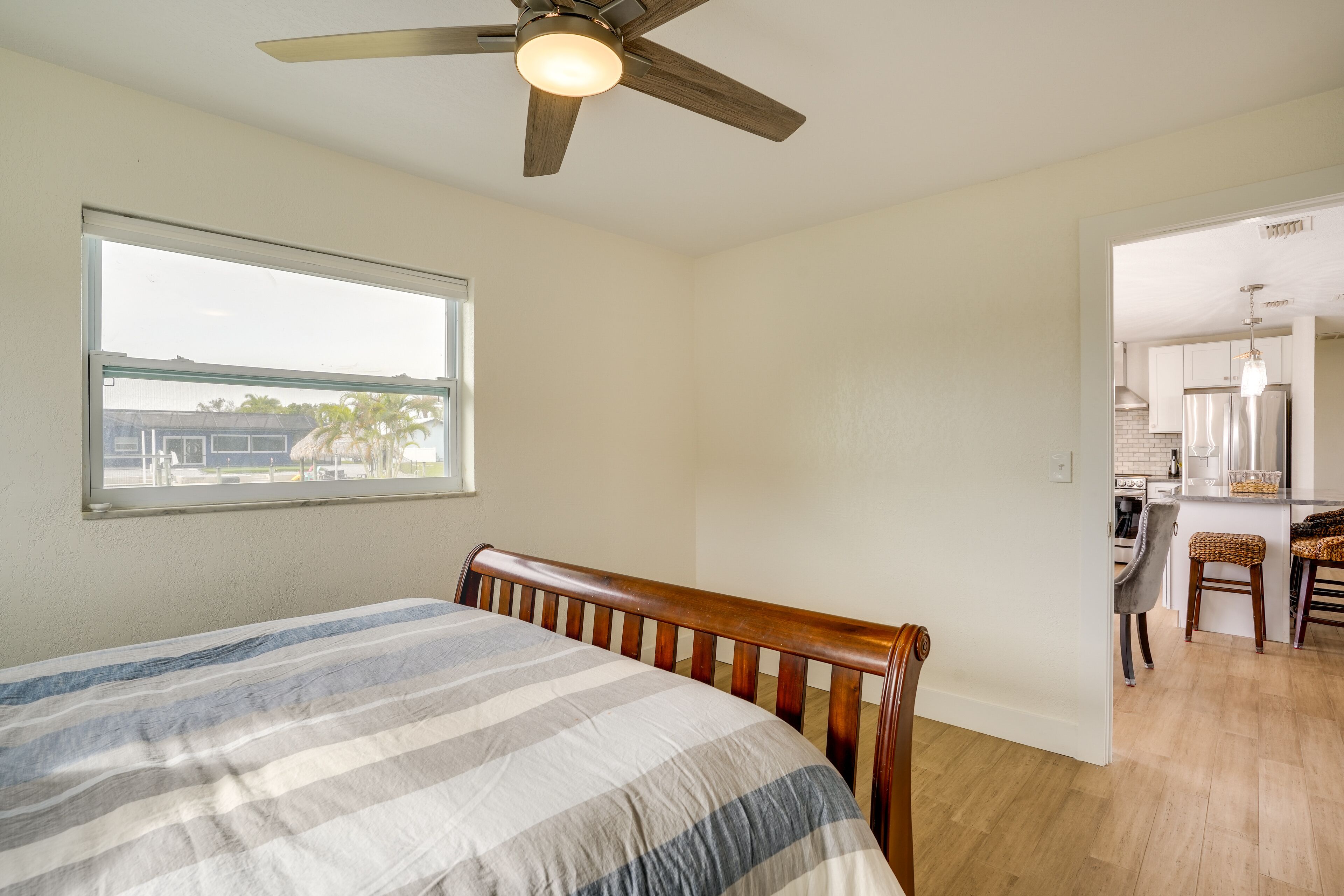 A bedroom with a bed, a ceiling fan, a window, and a view of the kitchen.