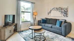 Ein modernes Wohnzimmer mit einem grauen Sofa, einem Holz-TV-Schrank, einem runden Couchtisch und einer Stehlampe.