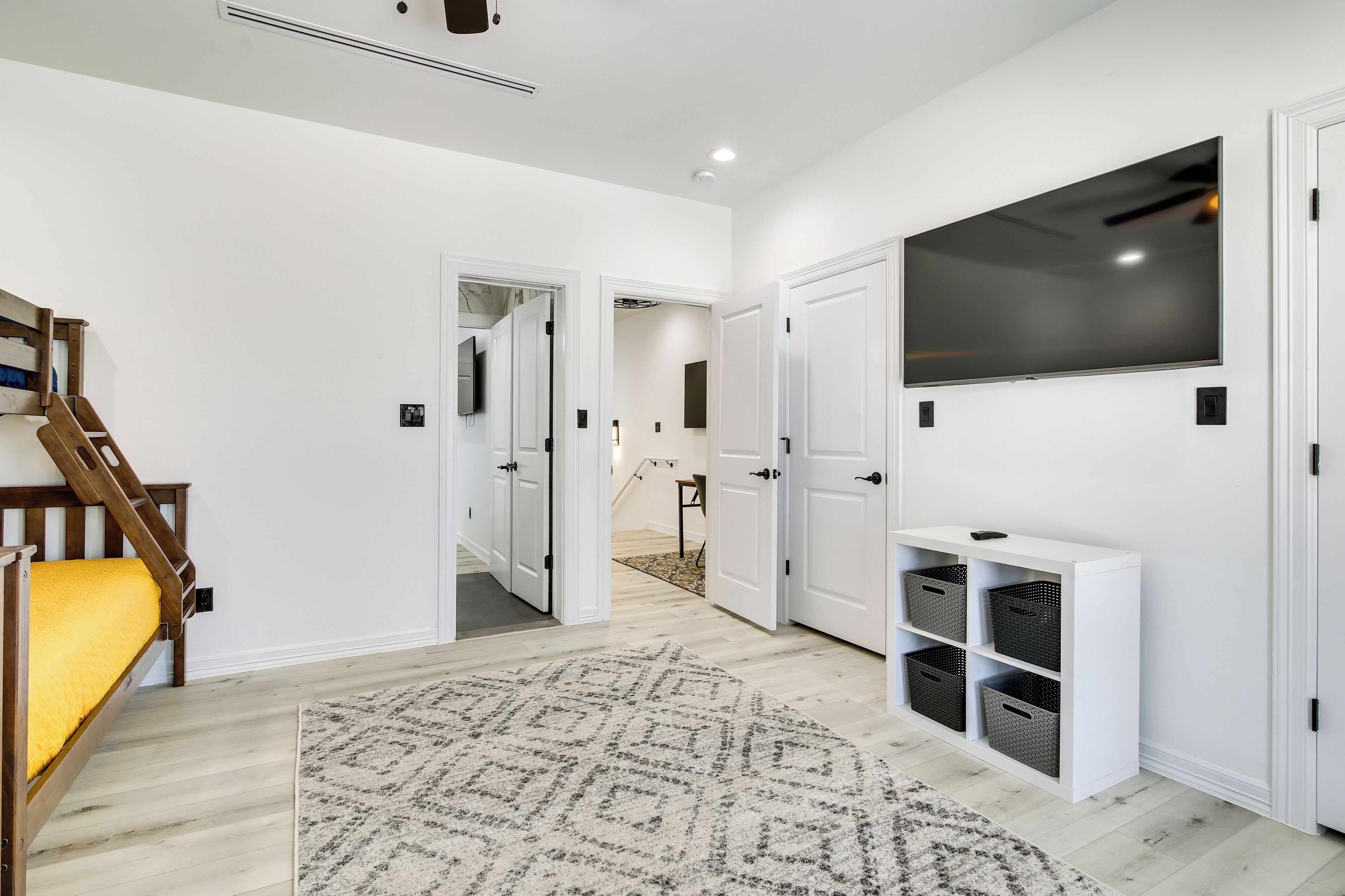A modern interior with a staircase, a large TV, and a white console unit with storage baskets.