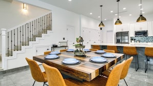 A modern kitchen with white cabinets, stainless steel appliances, and a wooden dining table set for six. - South Padre Island Retreat: Private Pool! (South Padre Island)