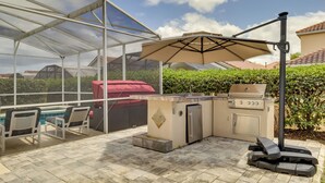 An outdoor patio with a grill, seating area, and a covered space. - Lanai & Pool: Spacious Villa Near Disney! (Davenport)