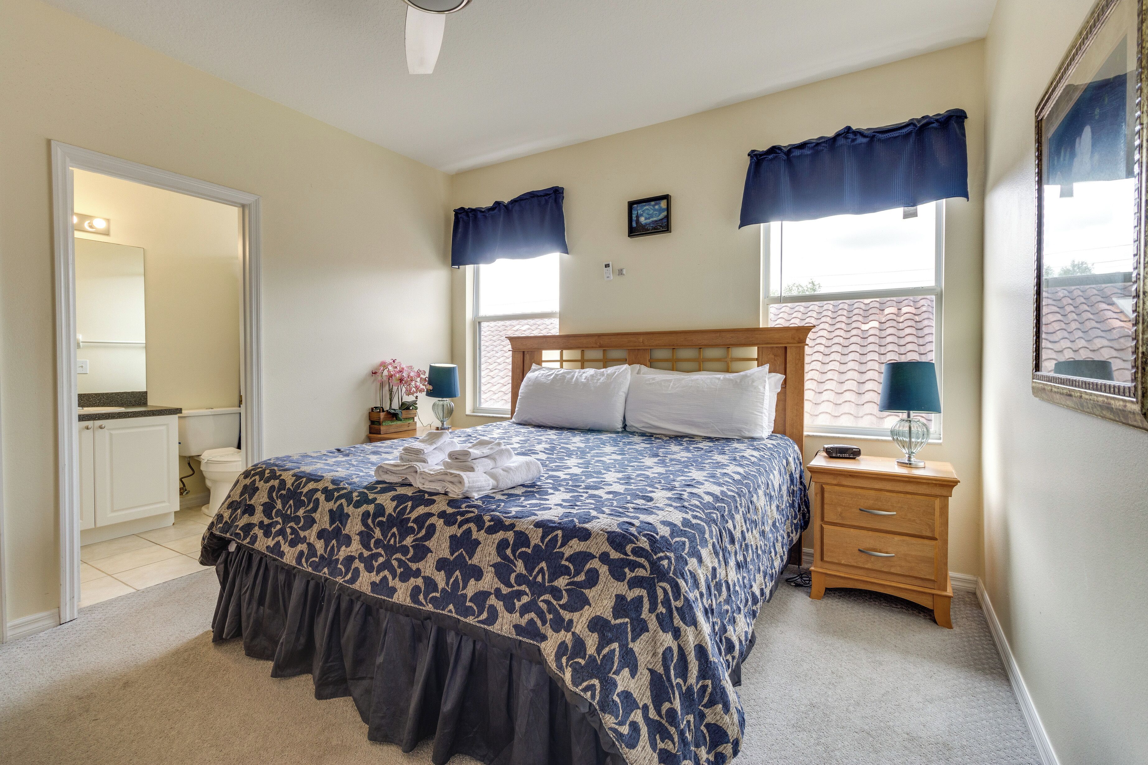 A bedroom with a bed, bedside tables, a nightstand, a window with curtains, a mirror, and a door leading to a bathroom.