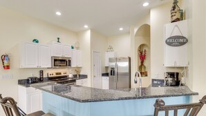 A kitchen with white cabinets, a granite countertop, a stainless steel refrigerator, and a 'Welcome Home' sign. - Lanai & Pool: Spacious Villa Near Disney! (Davenport)
