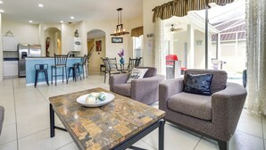A spacious living area with a kitchen in the background, a dining table with chairs, and a sofa with a decorative pillow. - Lanai & Pool: Spacious Villa Near Disney! (Davenport)