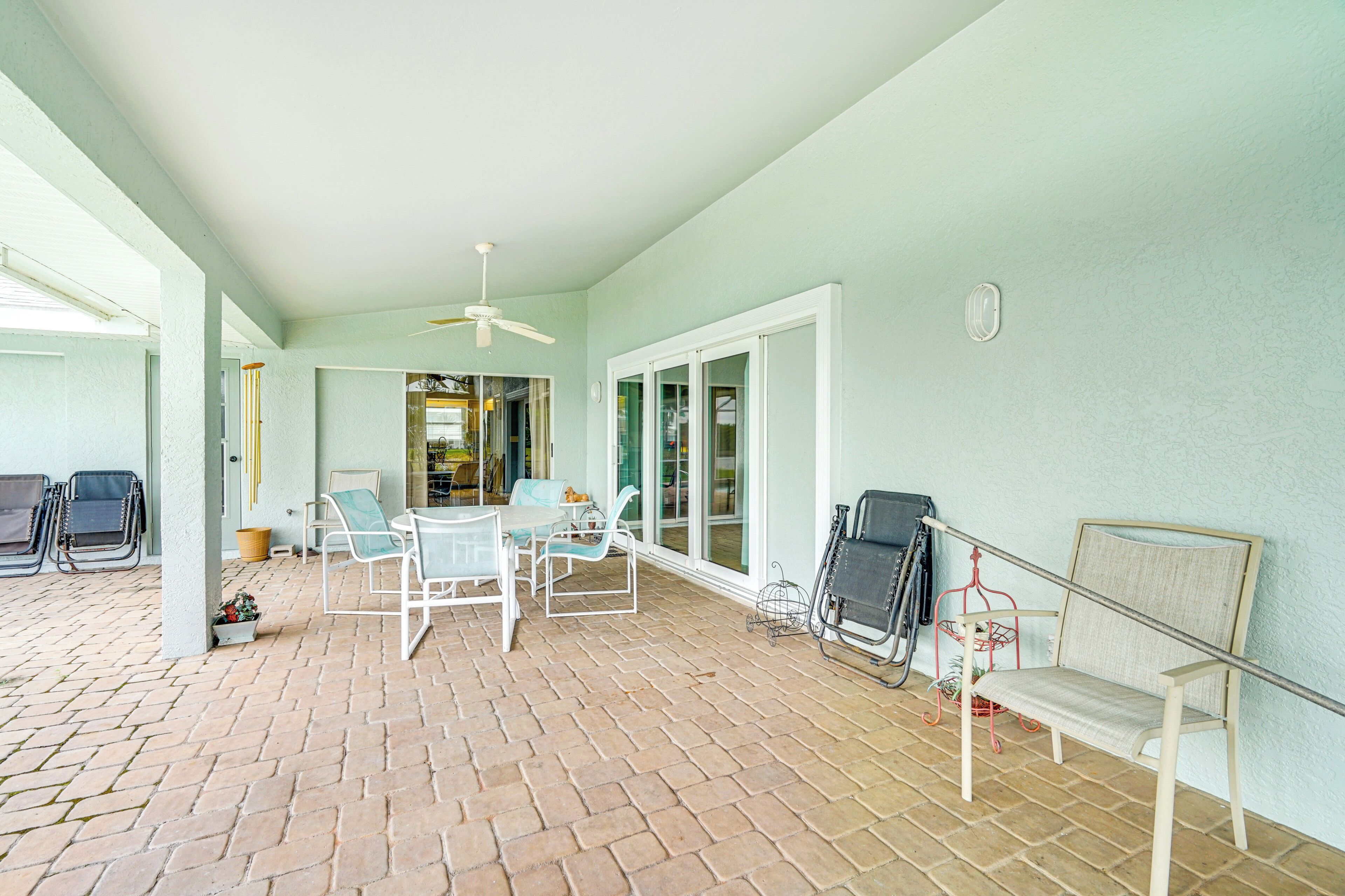 Un patio cubierto con piso de ladrillo, muebles blancos y un ventilador de techo.