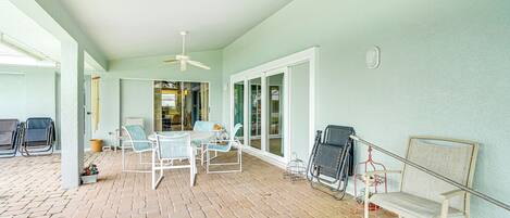 A covered patio area with a brick floor, white furniture, and a ceiling fan.