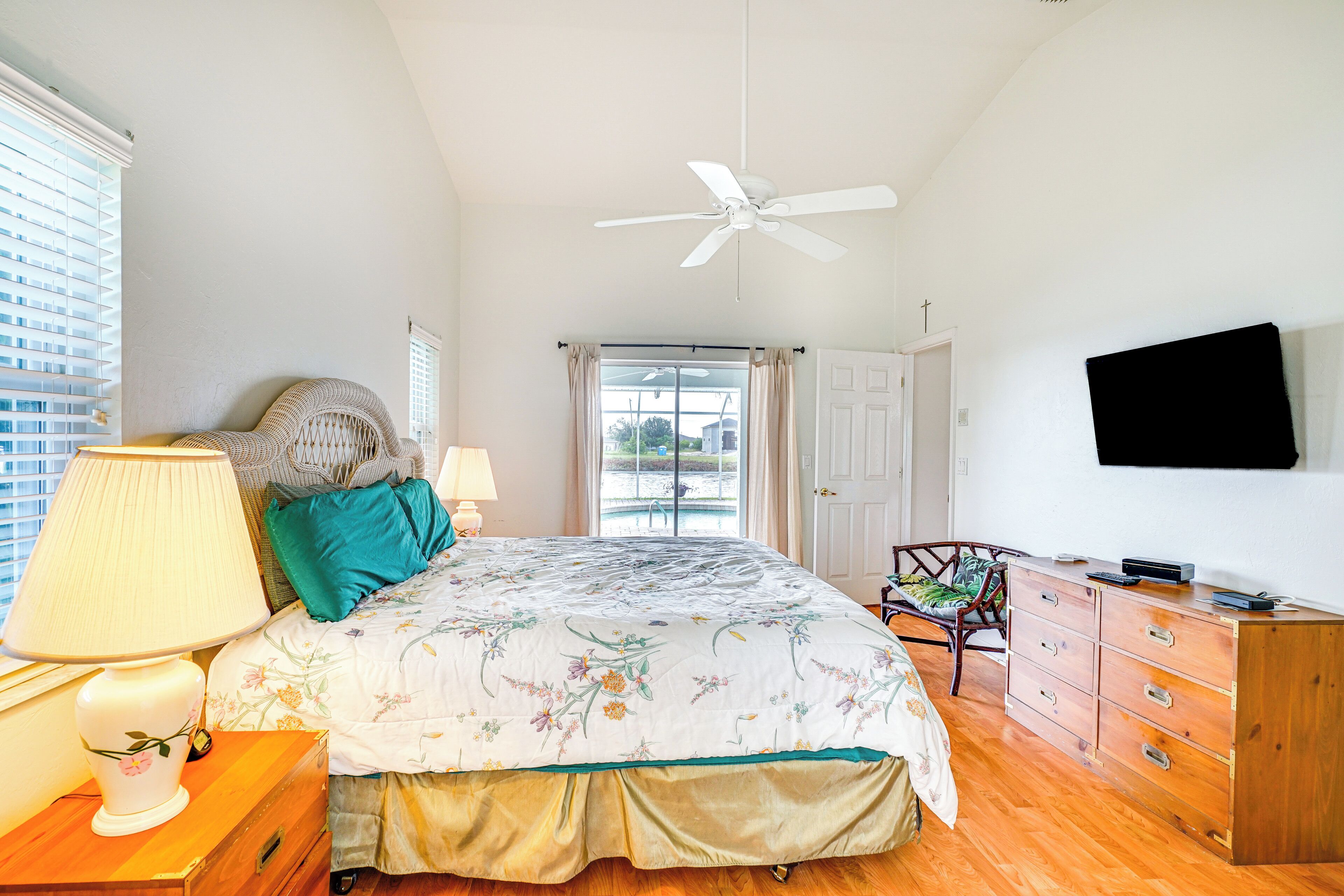 A bedroom with a bed, a nightstand, a dresser, a chair, a ceiling fan, and a TV mounted on the wall.