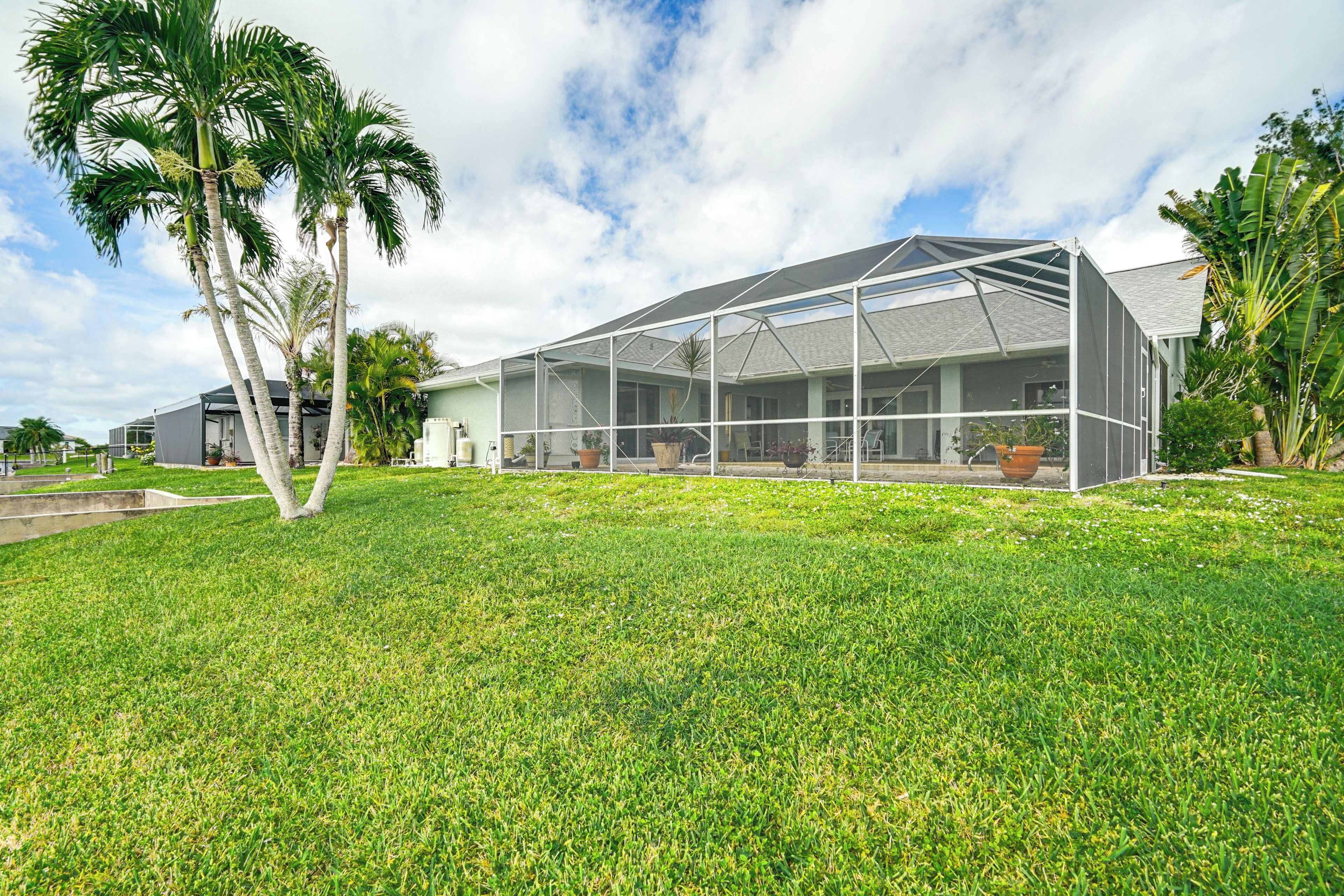 A modern house with a large covered patio area, surrounded by well-maintained grass and palm trees.